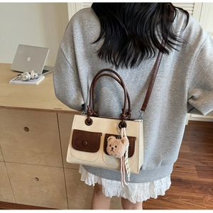 Model wearing a small square shoulder bag with a teddy bear charm in a lifestyle setting