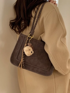 Retro brown suede tote bag with woven handles and plush dog charm on a model in wool coat