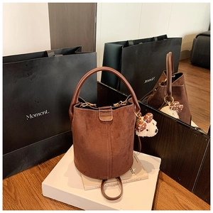 Detail einer braunen Wildleder-Beuteltasche mit Kontrastnähten und Bärenanhänger