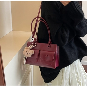 Detail of wine red square shoulder bag with front pockets and plush bear charm accessory