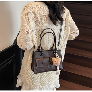Detail of vintage brown shoulder bag with double pockets and cute teddy bear charm