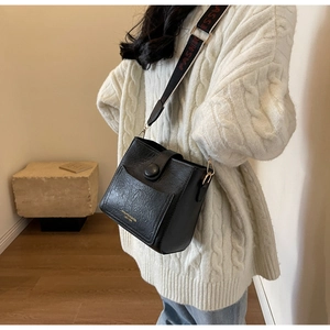 Sac seau noir avec texture plissée vintage et large bandoulière lettrée porté par le mannequin
