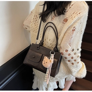 Detail view of square leather shoulder bag with two front pockets and plush bear charm