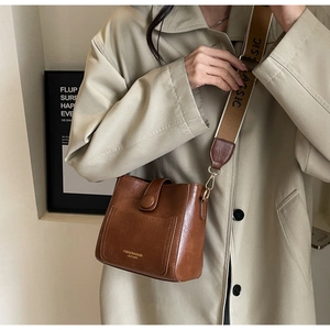Détail d'un sac seau en cuir marron avec large bandoulière et logo mode gaufré