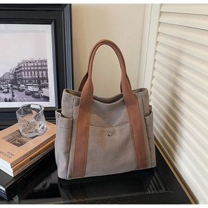 Canvas tote bag detail showing front snap pocket and side compartments on a sleek table