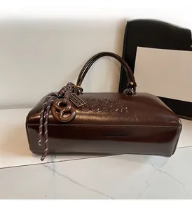 Close-up of chocolate brown pillow bag with textured leather and biscuit charm accessory