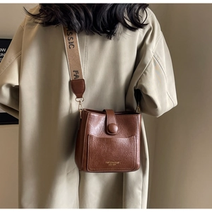Détail du sac seau en cuir marron avec texture rétro et bandoulière jacquard