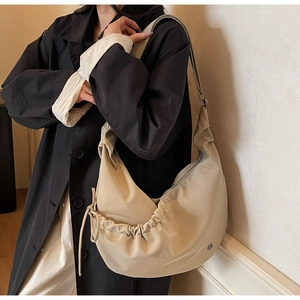 Beige large capacity pleated shoulder bag worn by model over a black trench coat