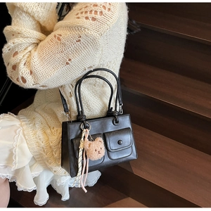 Detail view of black vintage leather crossbody bag with teddy bear charm on stairs