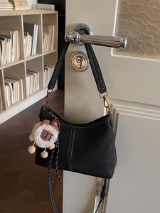 Sac à bandoulière noir avec coutures blanches et breloque ours sur une poignée