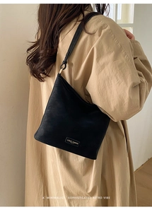 Minimalistische schwarze Retro-Umhängetasche getragen zu einem beigen Trenchcoat