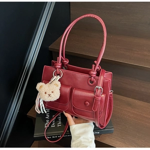 Detail of wine red square bag with double front pockets and a cute plush bear charm