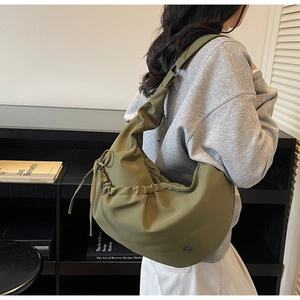 Detail of green nylon shoulder bag with drawstring folds and circular metal logo