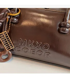 Detail of dark brown pillow bag with MKXQ embossed logo and gold abacus charm