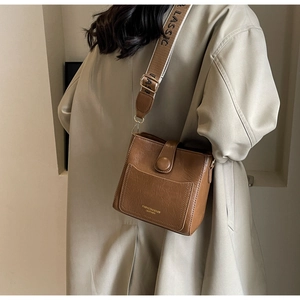 Détail du sac seau marron vintage avec lettrage doré et large bandoulière à logo