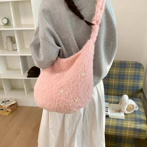 Detail of pink plush shoulder bag with star embroidery worn by a model in a cozy room