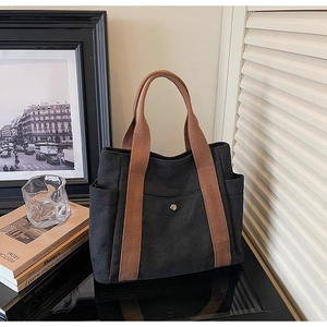Detail of black canvas tote bag with brown straps and side pockets on a vintage desk