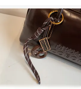 Macro view of retro dark brown leather bag showing gold abacus charm and letter embossing