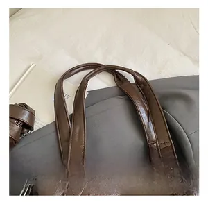 Detail view of wide double handles on a brown leather tote bag with silver hardware
