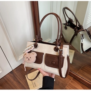 Detail of two-tone shoulder bag featuring brown front pockets and a cute teddy charm