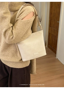 Detail einer cremeweißen Lederschultertasche mit Logo-Aufnäher und minimalistischem Gurt