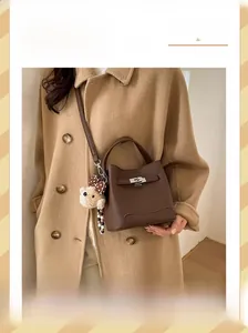 Detail of brown leather bucket bag featuring silver buckle and cute teddy bear charm