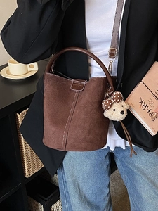 Braune Wildleder-Beuteltasche mit weißen Nähten und Bärenanhänger in Lifestyle-Szene