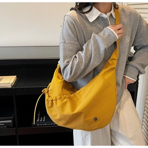Detail of yellow nylon dumpling bag featuring drawstring pleats and metal logo emblem