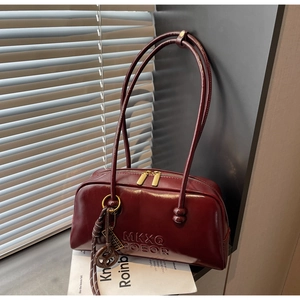Detail of burgundy glossy tote bag with dual gold zippers and decorative charms