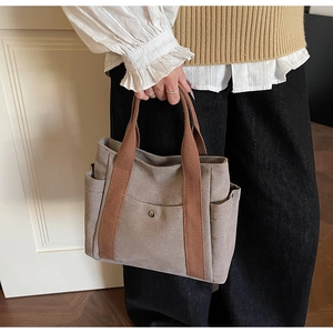 Detail of dark grey canvas tote bag featuring brown woven handles and front snap pocket