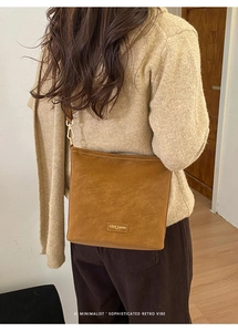 Braune Umhängetasche aus mattem Leder mit goldenem Logo über einem neutralen Strickpullover