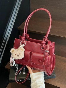 Deep red vintage square handbag with front pockets and cute bear charm on a wooden step