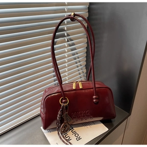 Detail of burgundy glossy leather shoulder bag with gold dual zippers and embossed lettering