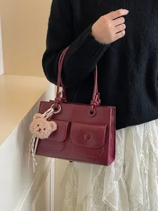Deep red leather rectangular handbag with dual front pockets and bear charm accessory
