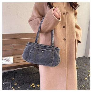 Close-up of a dark grey denim shoulder bag with frayed edges worn with a wool coat