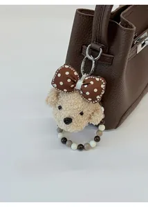 Detail of cute teddy bear plush charm with bead strap on a textured brown leather bucket bag