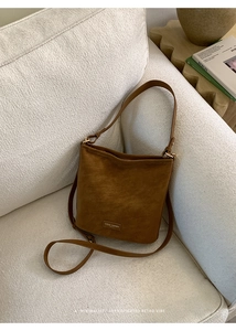 Detail einer braunen Vintage-Beuteltasche mit goldener Hardware auf weißem Plüschsofa