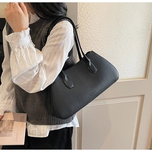 Close-up of black lychee textured leather tote bag worn on shoulder by a model