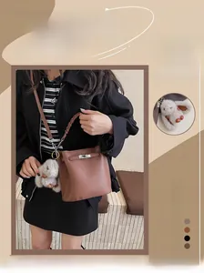 Détail du sac seau en cuir marron avec poignée tressée, boucle et pendentif lapin en peluche