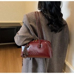 Detail of burgundy waxed leather shoulder bag with fine stitching and gold zipper closure