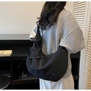 Close-up of black crossbody dumpling bag featuring pleated drawstring and metal logo
