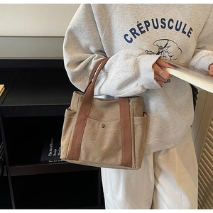Detail of khaki canvas tote bag with brown handles and snap button front pocket