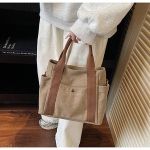Detail of khaki canvas tote bag with brown woven handles and metal snap button pocket