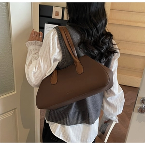 Deep brown leather tote bag detail with light brown straps worn by model in minimalist setting