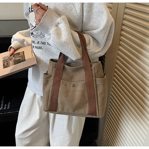 Detail of brown canvas tote bag featuring metal snap front pocket and side compartments