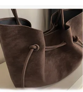 Detail of dark brown suede tote bag featuring adjustable drawstring and knot decorative element