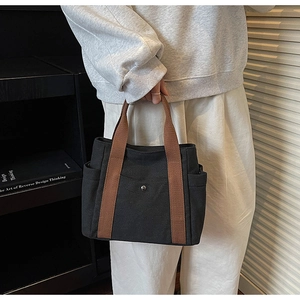 Detailed view of black canvas tote bag with brown woven handles and multi-pocket design
