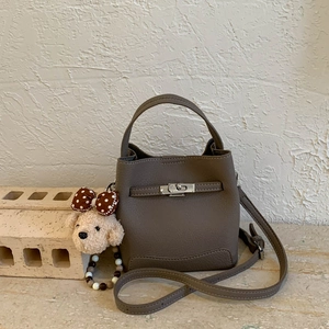 Detail view of brown pebbled leather bucket bag with silver clasp and teddy bear charm