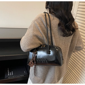 Detail of black patent leather shoulder bag featuring embossed lettering and gold zippers