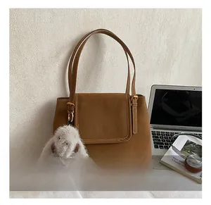 Détail d'un sac seau rétro marron avec pendentif lapin et logo doré sur un décor de lit
